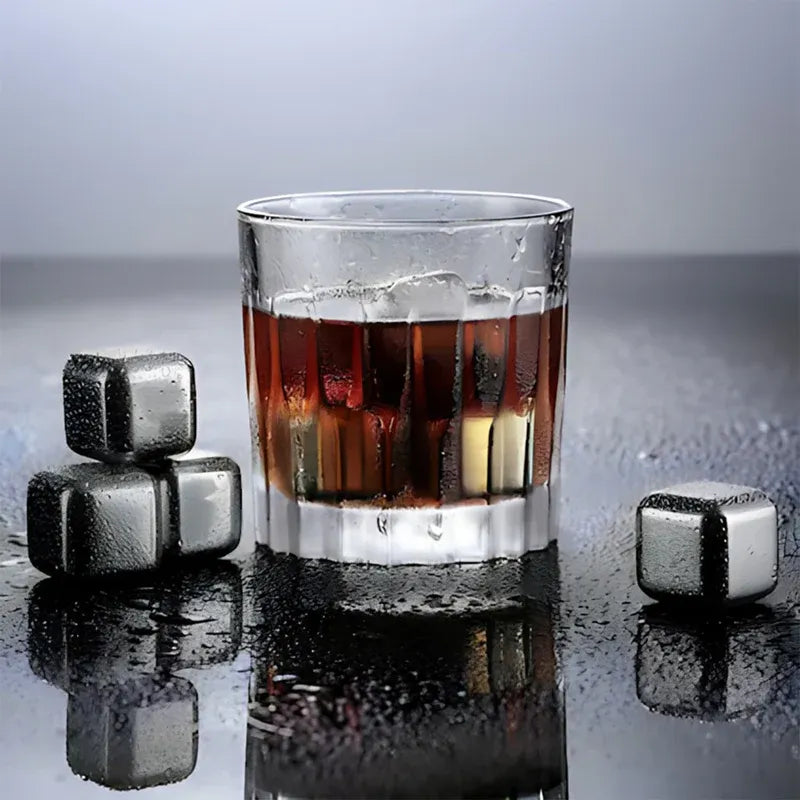 Glass of whiskey with ice cubes and metal stones on a reflective surface
