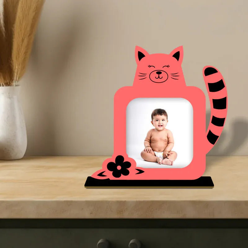 Pink cat-shaped photo frame with a baby picture on a wooden surface.
