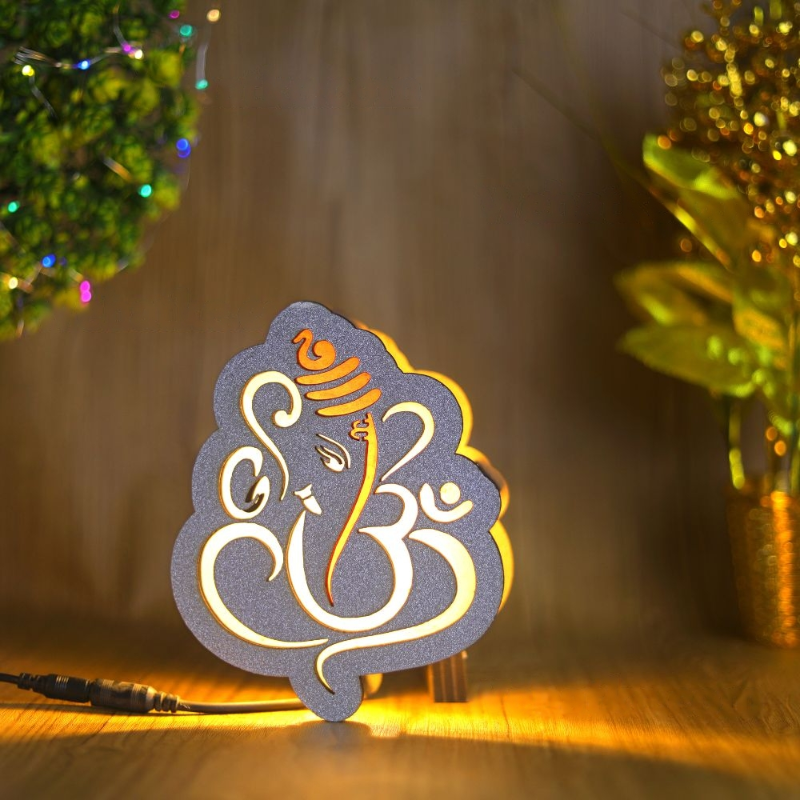 An illuminated LED lamp with a depiction of Lord Ganesha, emitting a warm glow, placed on a wooden surface.