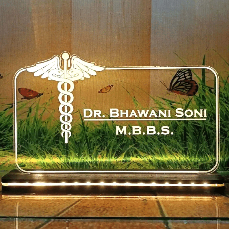 A customized LED name lamp with a 3D effect design featuring a medical theme, with the name 'Dr. Bhawani Soni' and 'MBBS' on the front, placed on a table.