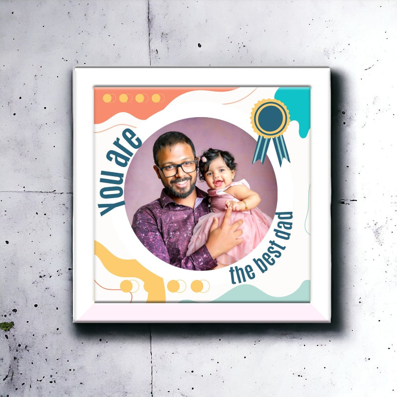 A custom wooden photo frame with a colorful design, featuring a photo of a father and his daughter, with a textual message that reads 'You are the best Dad'.