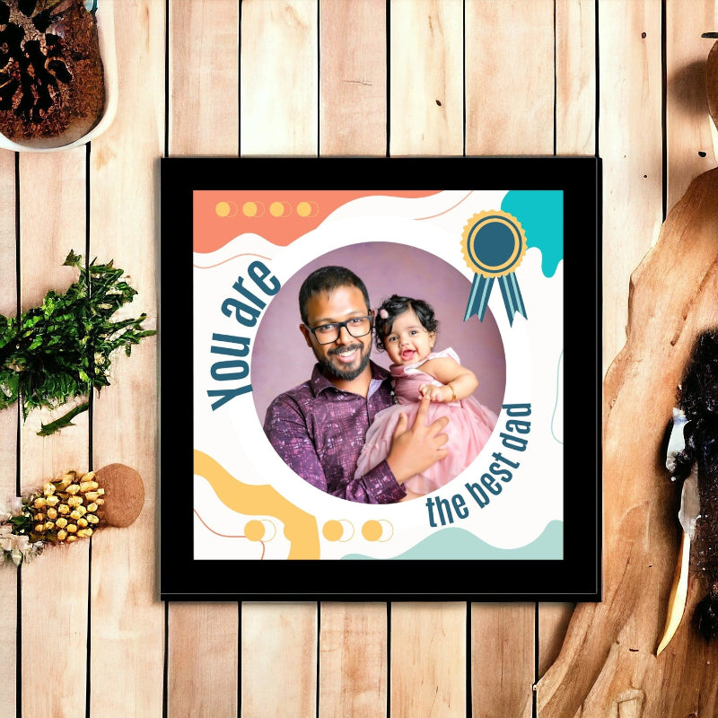 Framed picture of a man holding a child with 'You are the best dad' text on a wooden surface.