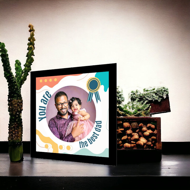 Framed picture of a man and a child with text 'You are the best dad' on a table with plants in the background.