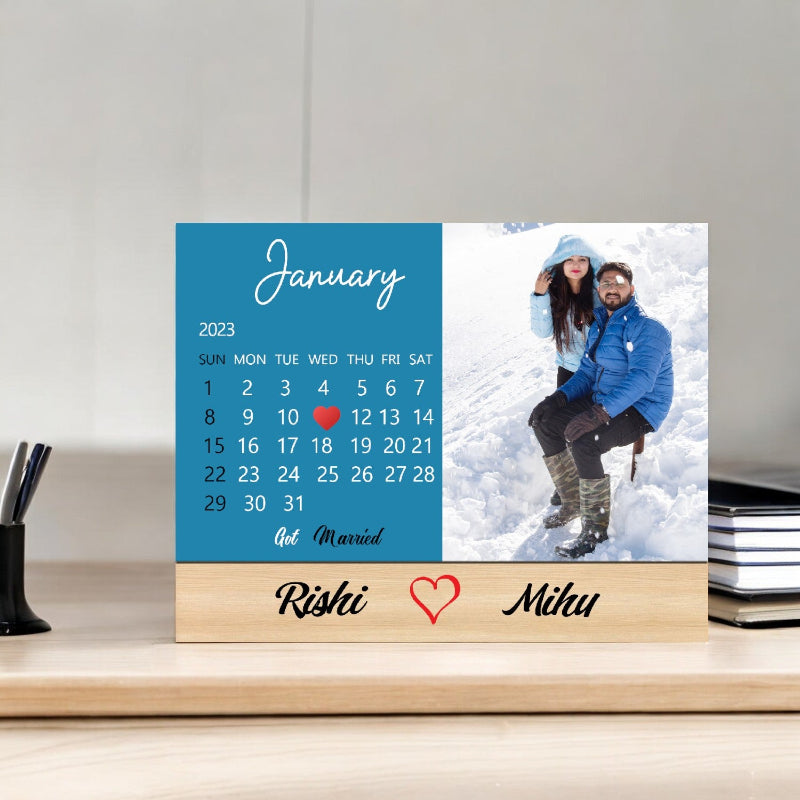 Personalized calendar with a couple's photo and names on a wooden stand.