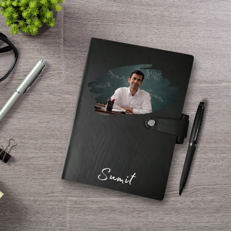 Black notebook with a photo of a man and the name 'Sumit' on a wooden surface with office supplies.