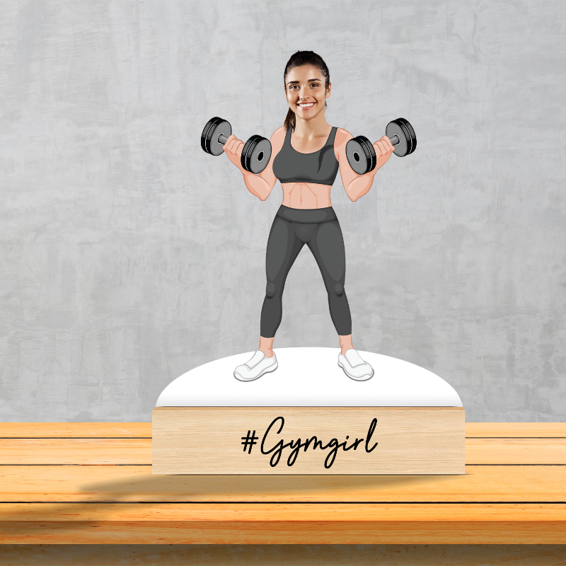 A personalized caricature of a female gym enthusiast, depicted with weights and in a fitness pose, placed on a wooden surface with the hashtag '#GYMGIRL'.