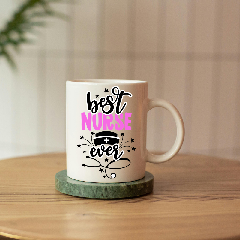 A white ceramic mug with pink and black text reading 'Best Nurse Ever' and decorative elements, placed on a wooden surface.
