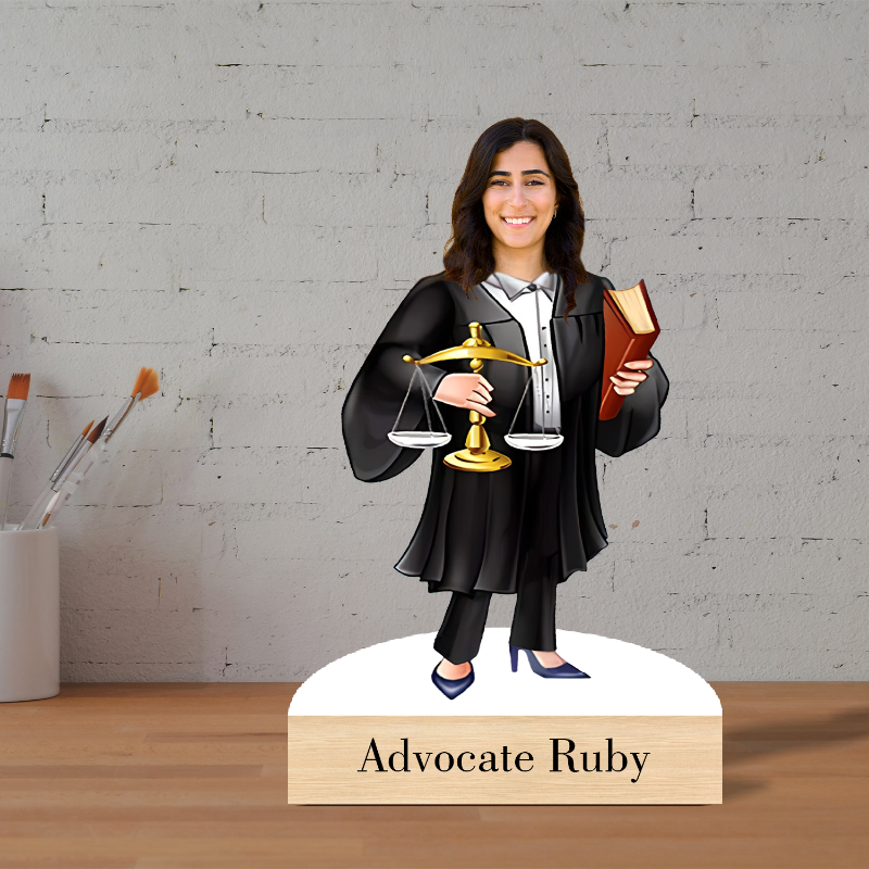 Figurine of a lawyer holding scales and a book on a wooden base with 'Advocate Ruby' text, against a gray brick wall.