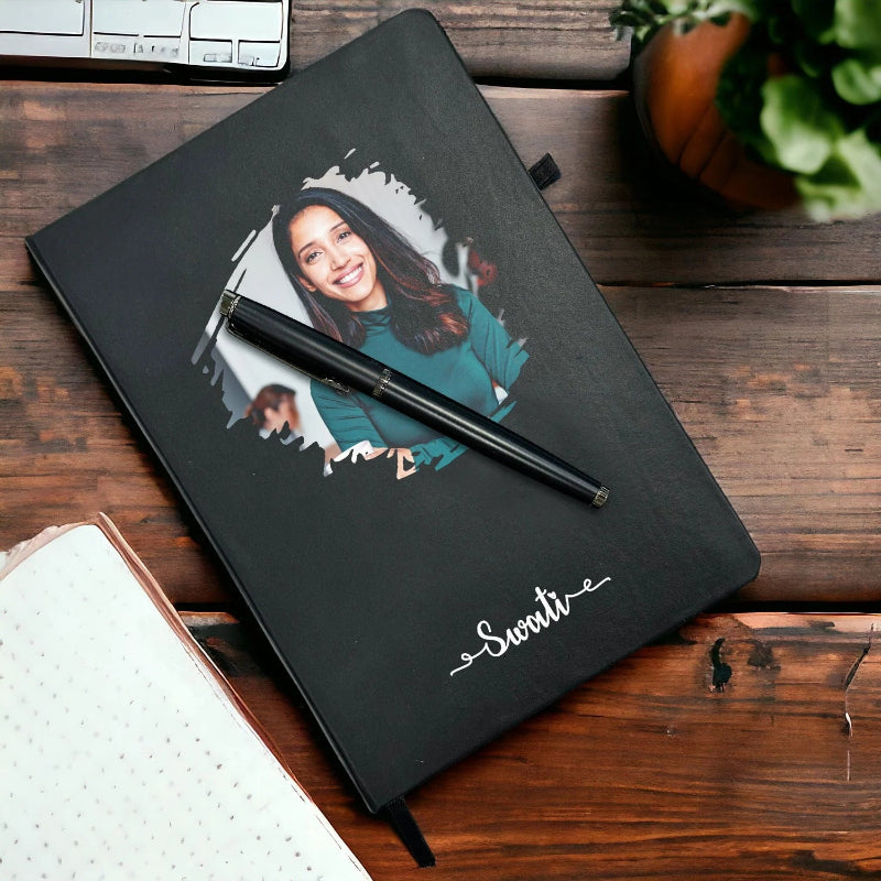 A personalized black photo journal and pen set with a printed picture of a woman on the cover, placed on a wooden table.
