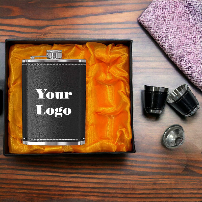 Black flask with 'Your Logo' text in a box on a wooden surface with shot glasses and a towel.