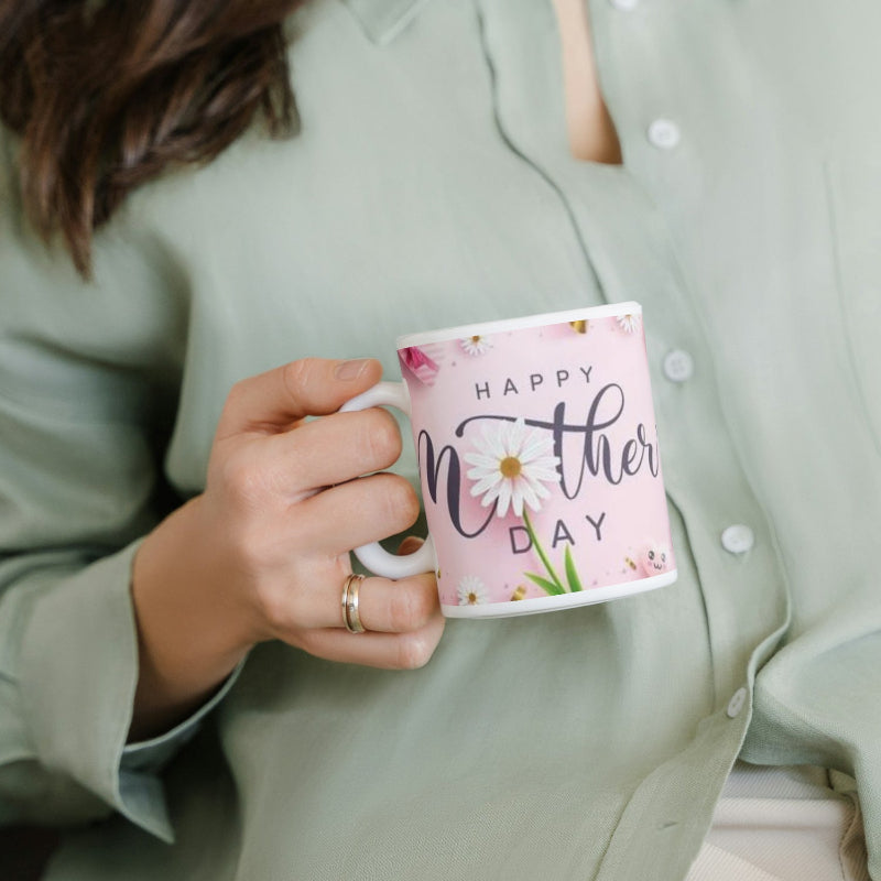 A person holding a pink ceramic mug with floral designs and the text 'HAPPY MOTHER DAY' on it.