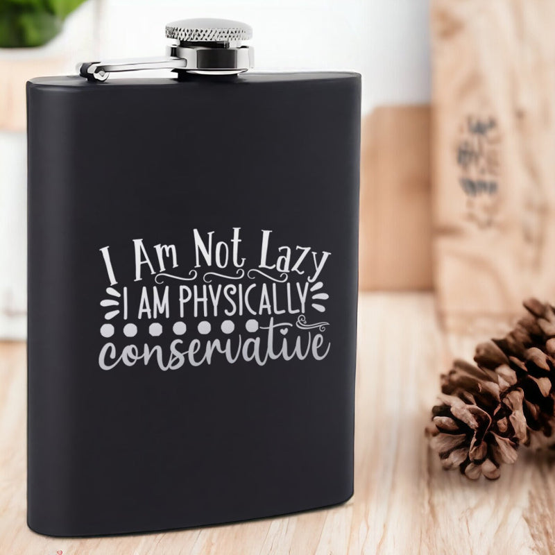 Black flask with humorous text on a wooden surface with pine cones.
