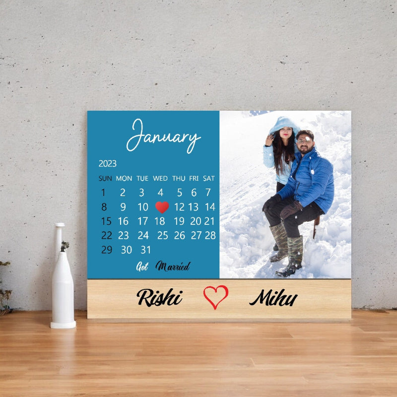 Personalized calendar with a couple's photo and names on a wooden stand against a gray wall.