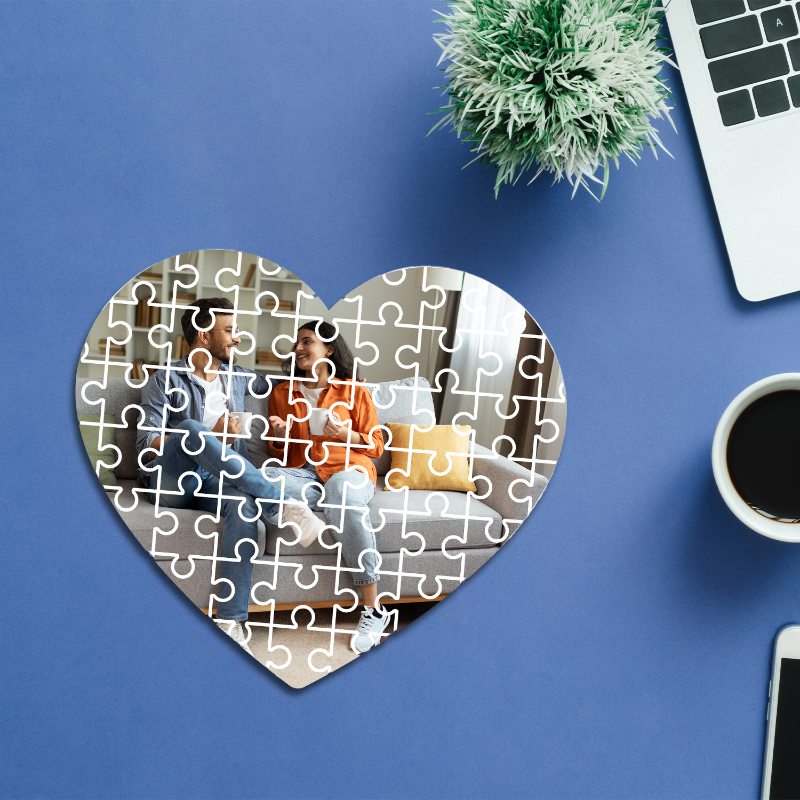 Heart-shaped puzzle with a couple on a blue desk with a laptop and coffee.