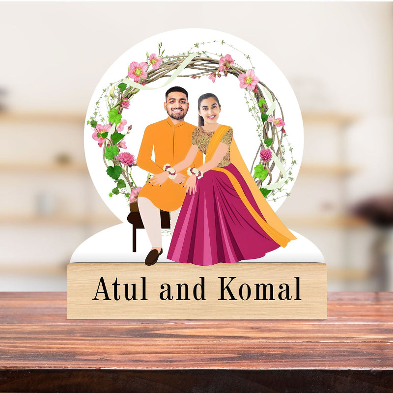 Decorative piece with a couple's illustration and floral wreath, placed on a wooden block with 'Atul and Komal' text.