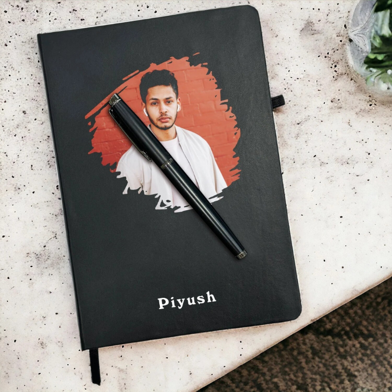 Black notebook with a portrait of a person on the cover and a pen on a textured surface