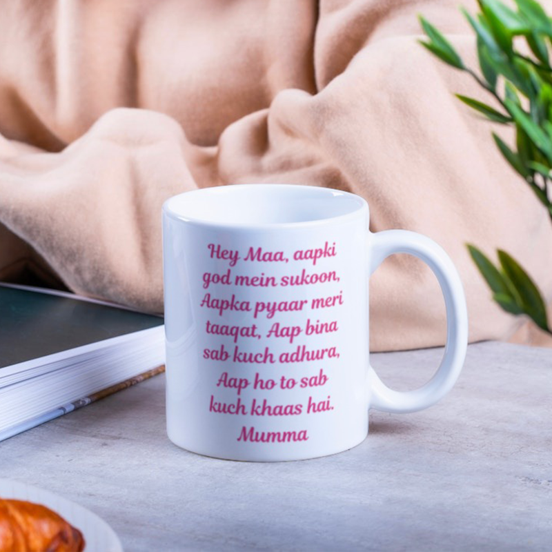 White mug with pink text on a wooden surface with a blurred background