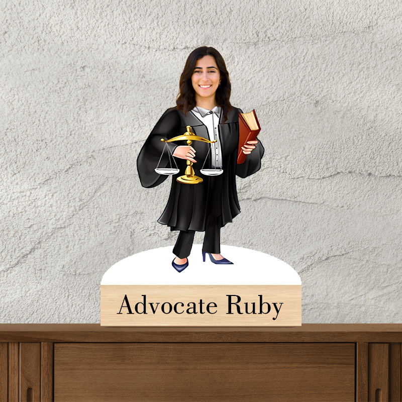 Figurine of a woman in a lawyer's robe holding a scale and a book, with a nameplate below on a wooden surface.
