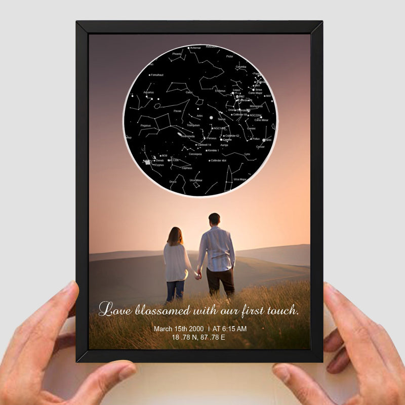 Framed artwork with a couple in a field and star map, held by hands.