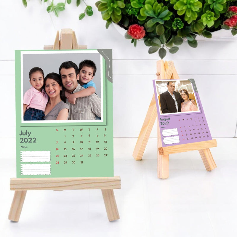 A custom photo calendar for 2022, personalized with family photos, displayed on a desk with a sturdy wooden stand. The calendar is predominantly green with a photo frame design and includes a sturdy stand.