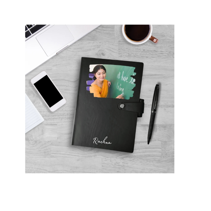 Black notebook with a personalized name on a desk with a phone, coffee cup, and pen.