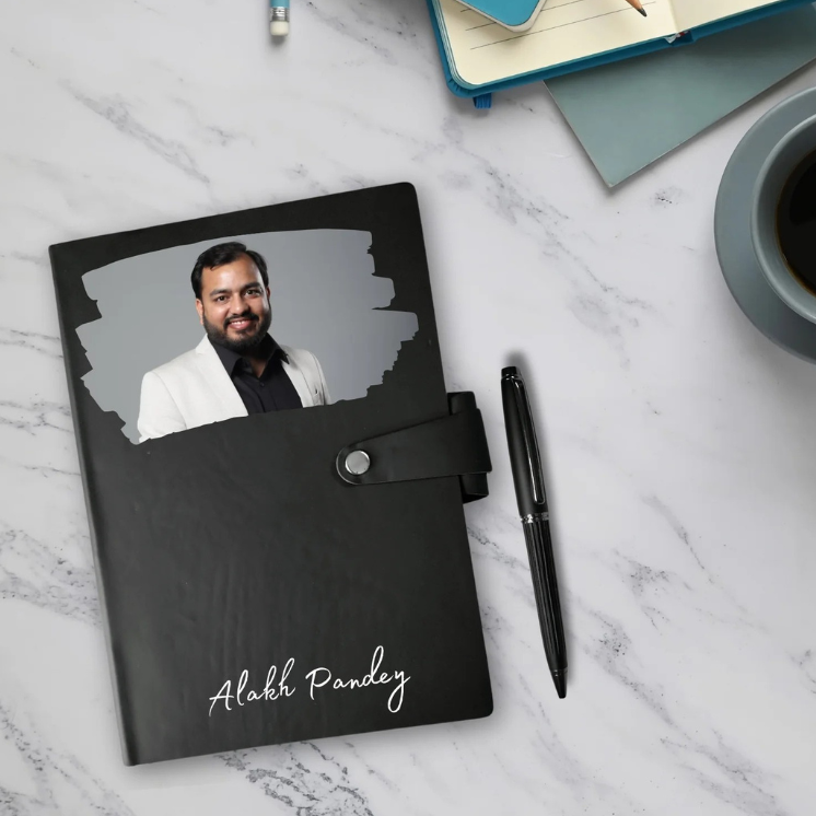 Black notebook with a photo of a man on the cover, placed on a marble surface with a pen and coffee cup.
