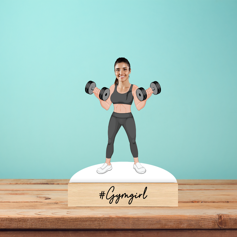 Figurine of a woman lifting weights with '#Gymgirl' text on a wooden base against a light blue background