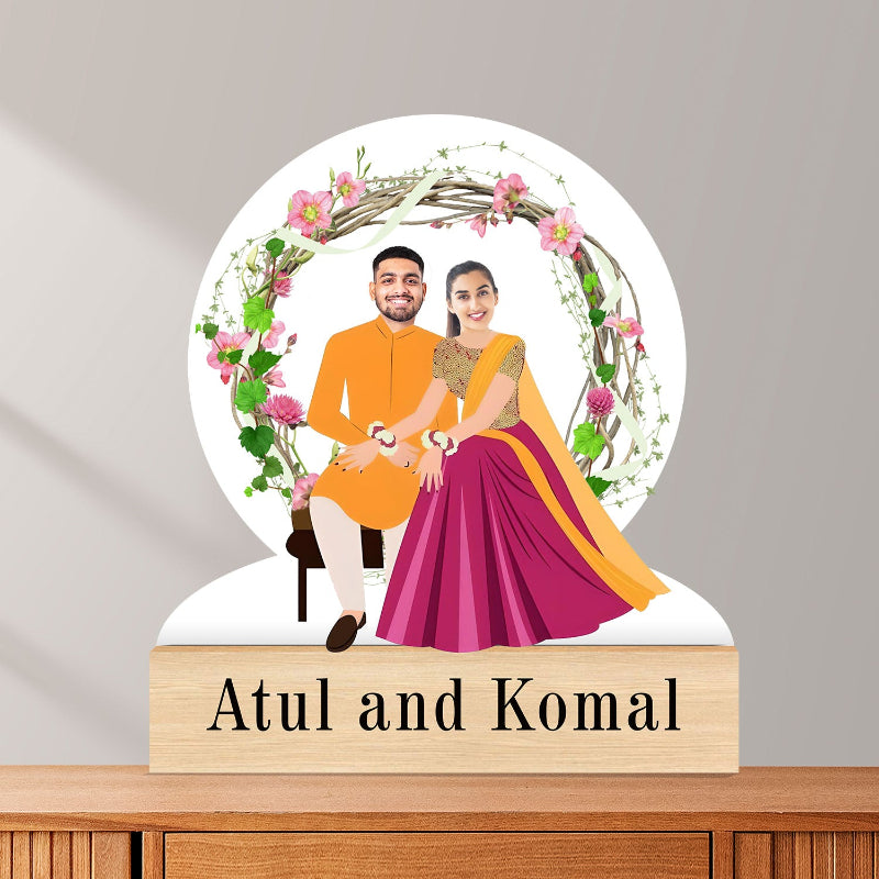 Decorative display with a couple in traditional attire and floral design, on a wooden base with 'Atul and Komal' text.
