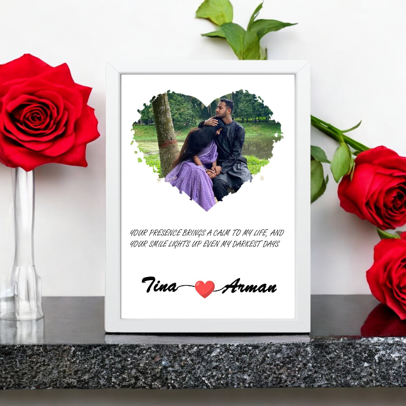 A wooden picture frame with a heart-shaped window displaying a couple's photo, surrounded by red roses.