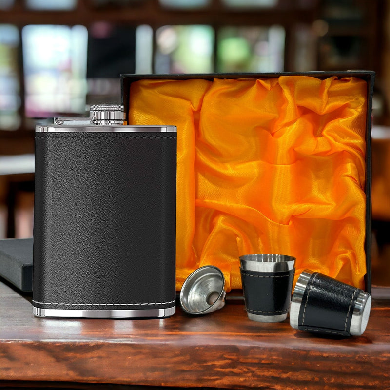 Black leather flask with silver accents and two matching shot glasses on a wooden surface.