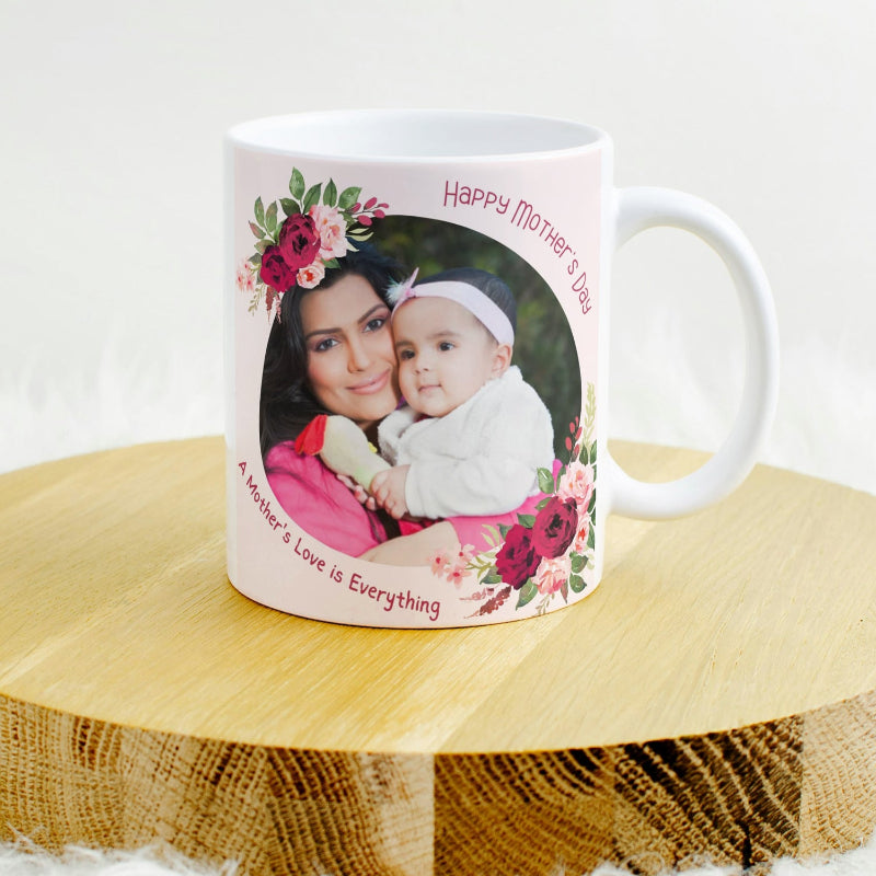 A white ceramic coffee mug with a photo printed on it, showing a mother and her child, adorned with a floral pattern and text celebrating Mother's Day.