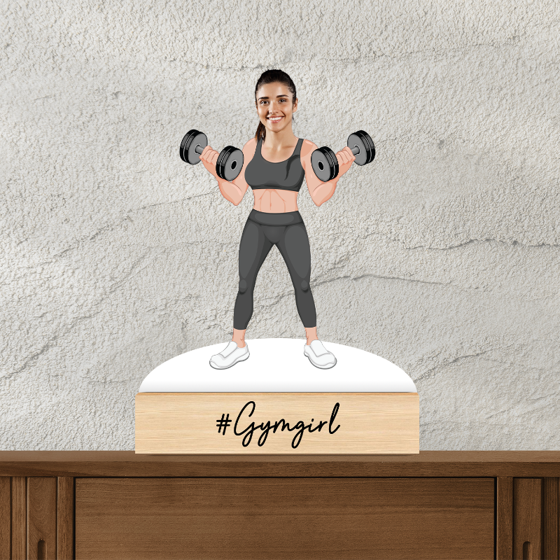 Figurine of a woman lifting weights with '#Gymgirl' text on a wooden base against a textured wall.