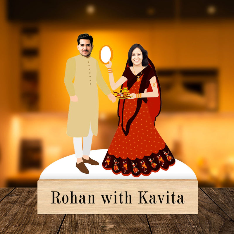 A custom-made caricature of a couple, with the man in a beige suit and the woman in a red and black dress, standing on a wooden platform with the text 'ROHAN WITH KAVITA' below them.