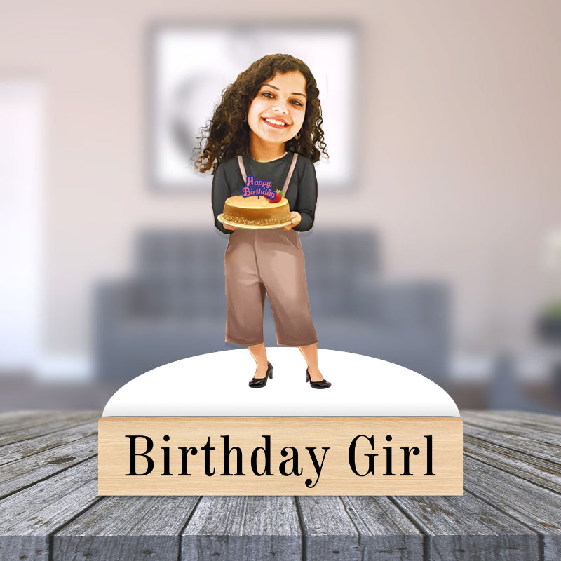 caricature of a girl holding a cake with 'Happy Birthday' on a wooden base, set against a blurred indoor background.