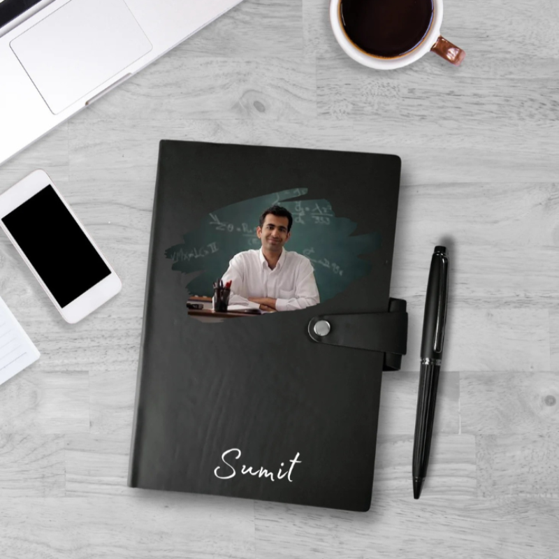 Black notebook with a photo of a man and the name 'Sumit', placed on a desk with a phone, pen, and coffee cup.