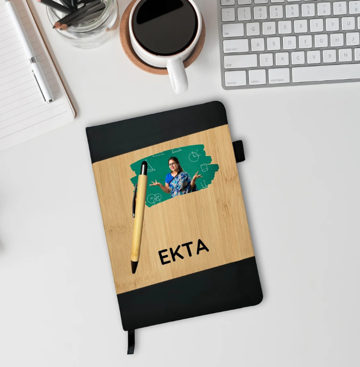 Notebook with wooden cover and black top, pen, and photo on a desk.