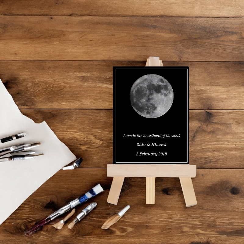 Moon phase print on a wooden easel with paintbrushes and paper on a wooden surface