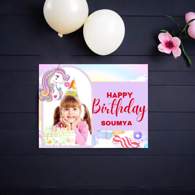 Personalized birthday card with a child's photo and unicorn design on a dark wooden surface.