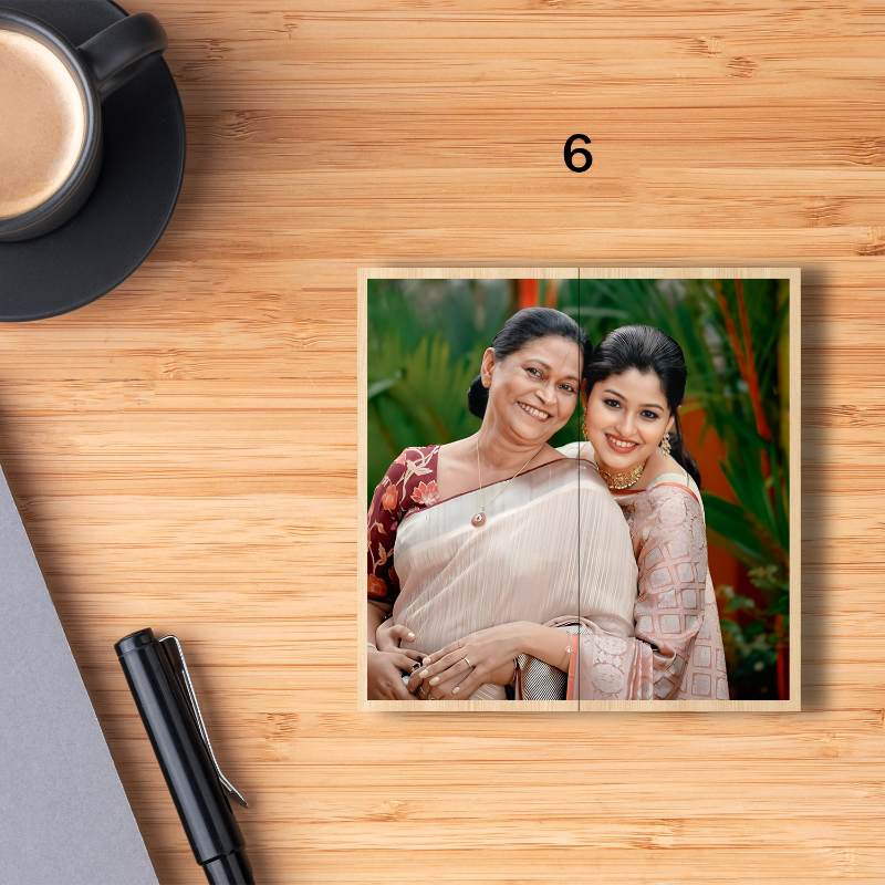 Two women hugging with a photo frame on a wooden surface, next to a cup of coffee and pen.