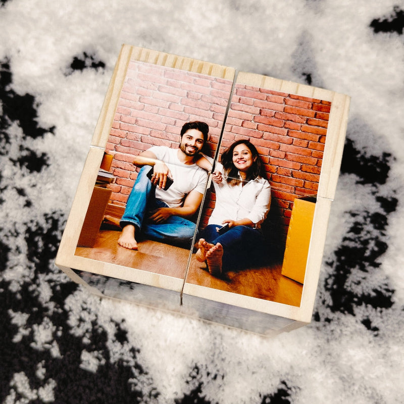 A wooden rolling photo cube with a couple's photo on it, placed on a black surface with snow-like flakes around.