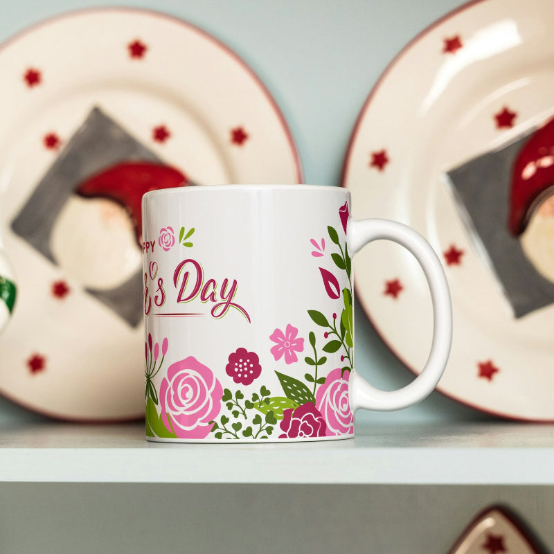 White mug with floral design and 'Happy Mother's Day' text, placed on a shelf with decorative plates in the background.