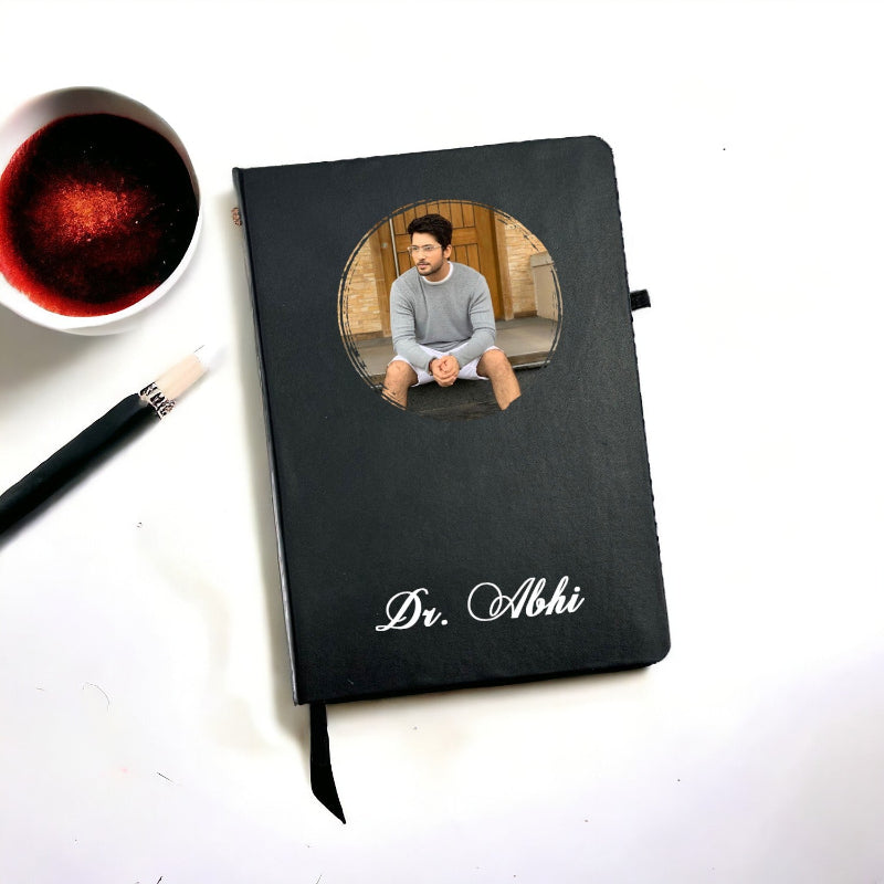 A custom photo diary for doctors with a black cover, a personalized photo of a doctor on the front, a pen, and a cup of coffee on the side.