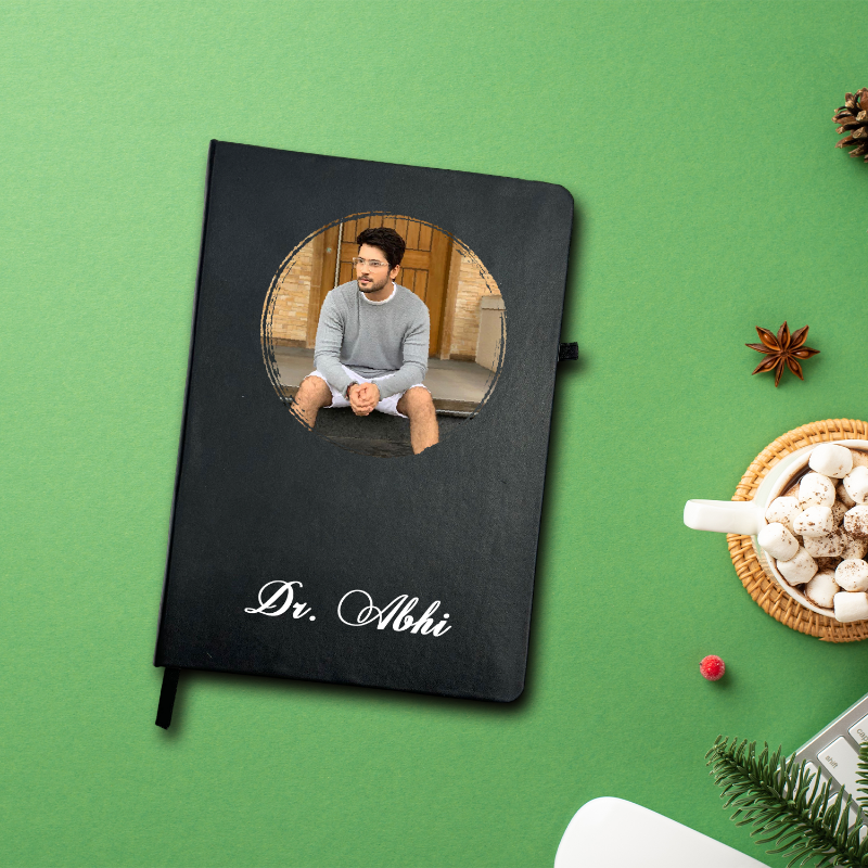 Black notebook with a photo of a person on the cover, placed on a green surface with decorative items.