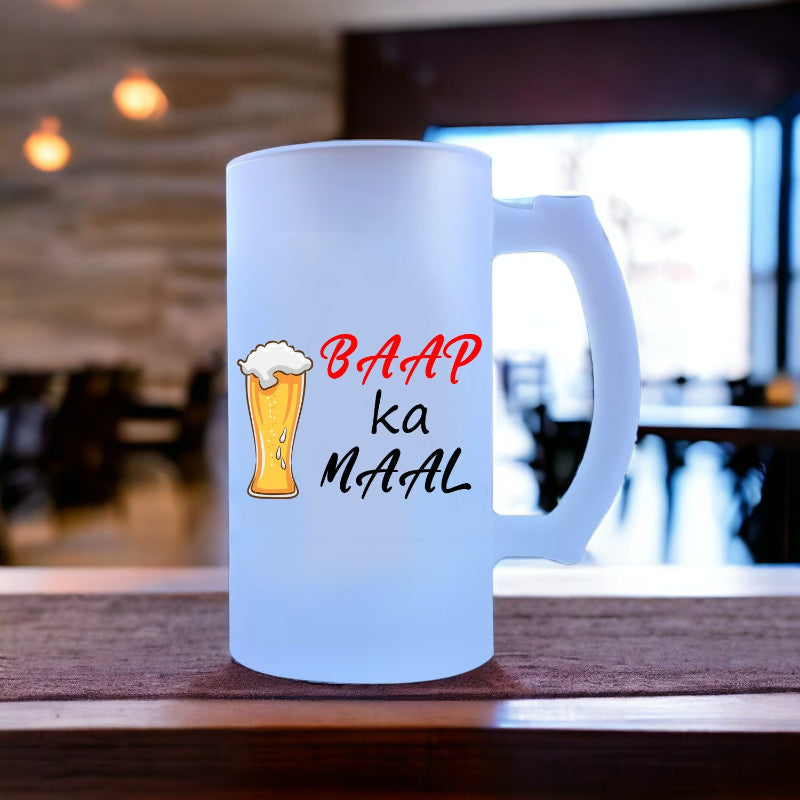 A blue glass beer mug with 'BAAP KA MAAL' printed in red text, placed on a wooden surface in a restaurant setting.