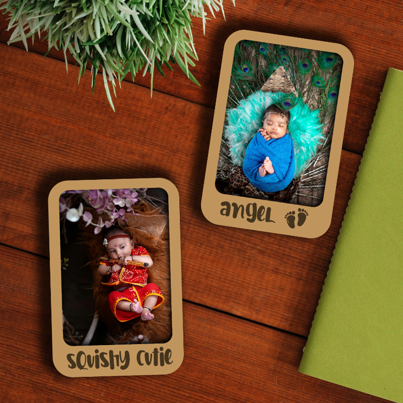 Two personalized wooden fridge magnets with one showing a baby in a blue dress and the other showing a baby in a yellow and red outfit, both with personalized text.