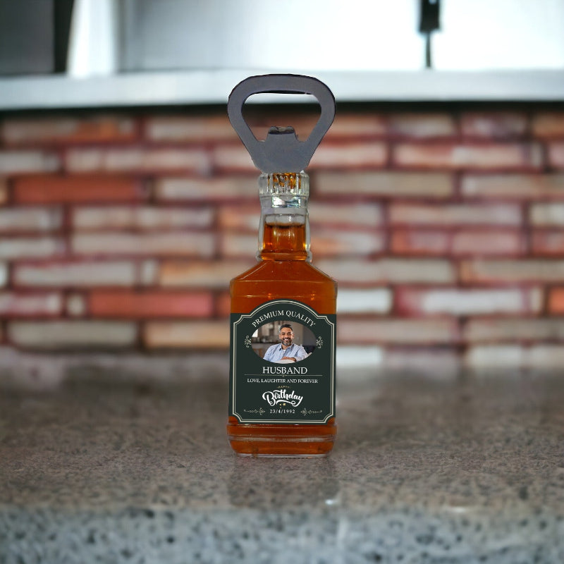 Bottle of whiskey with a bottle opener on top, labeled 'Husband', against a brick wall background.