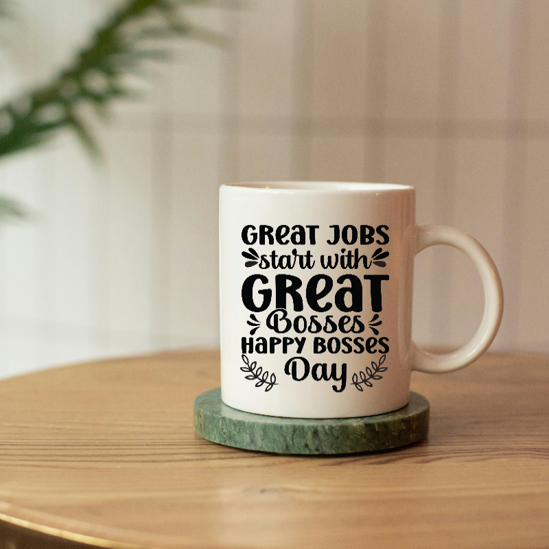 A white ceramic coffee mug with printed text 'GREAT JOBS start with GREAT Bosses & Happy Bosses Day' placed on a green coaster.