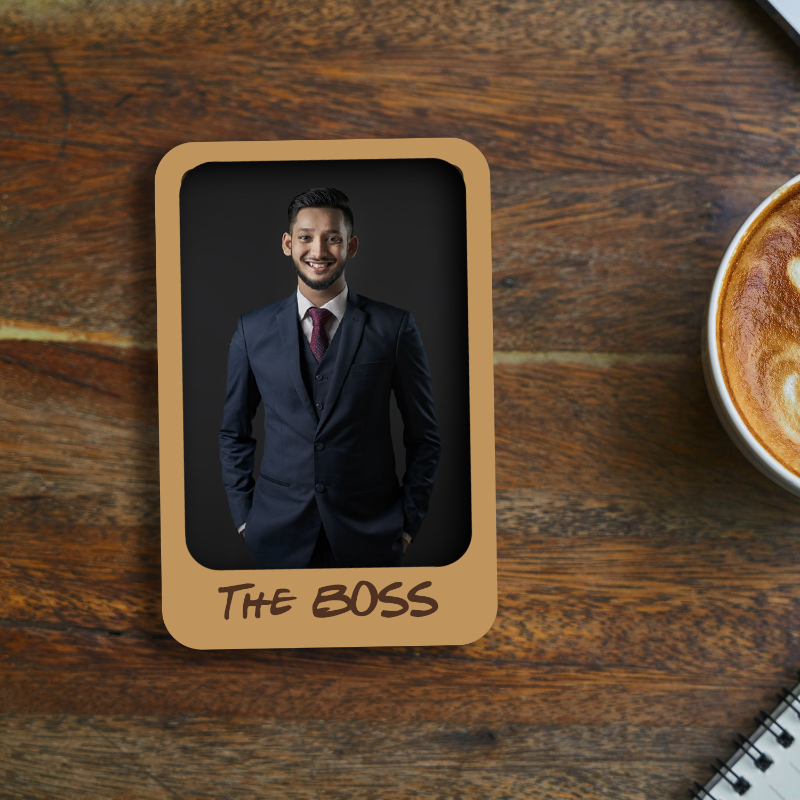 Framed photo of a man in a suit labeled 'The Boss' on a wooden surface with a coffee cup.