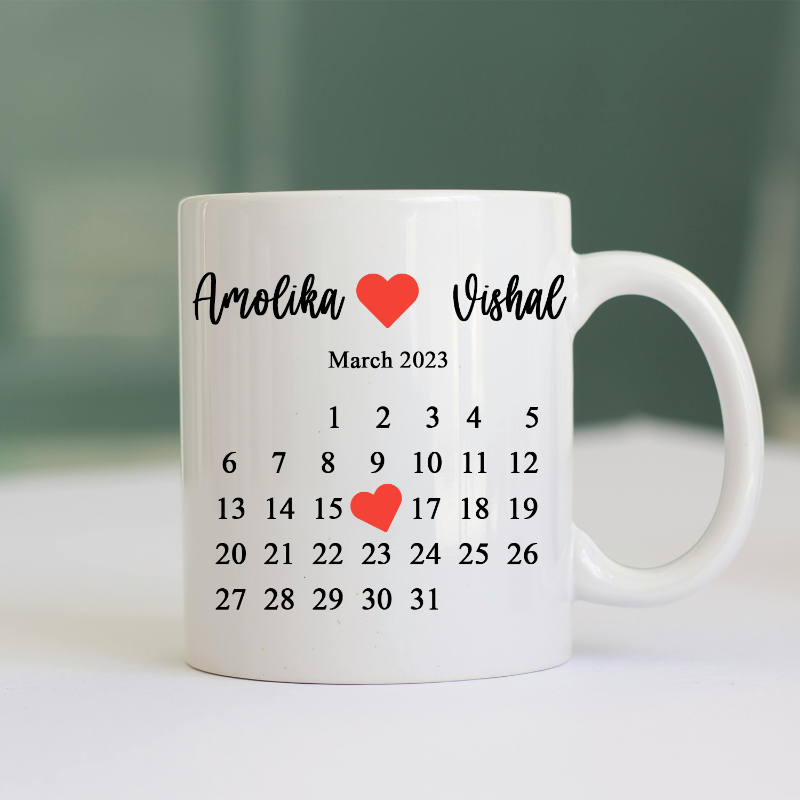 A white ceramic coffee mug with a personalized print. The print includes a calendar for March 2023, names, and a heart symbol, all in black and red colors.