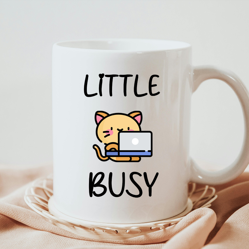 A white ceramic coffee mug with a printed design featuring a cartoon image of a cat and the text 'LITTLE BUSY'.